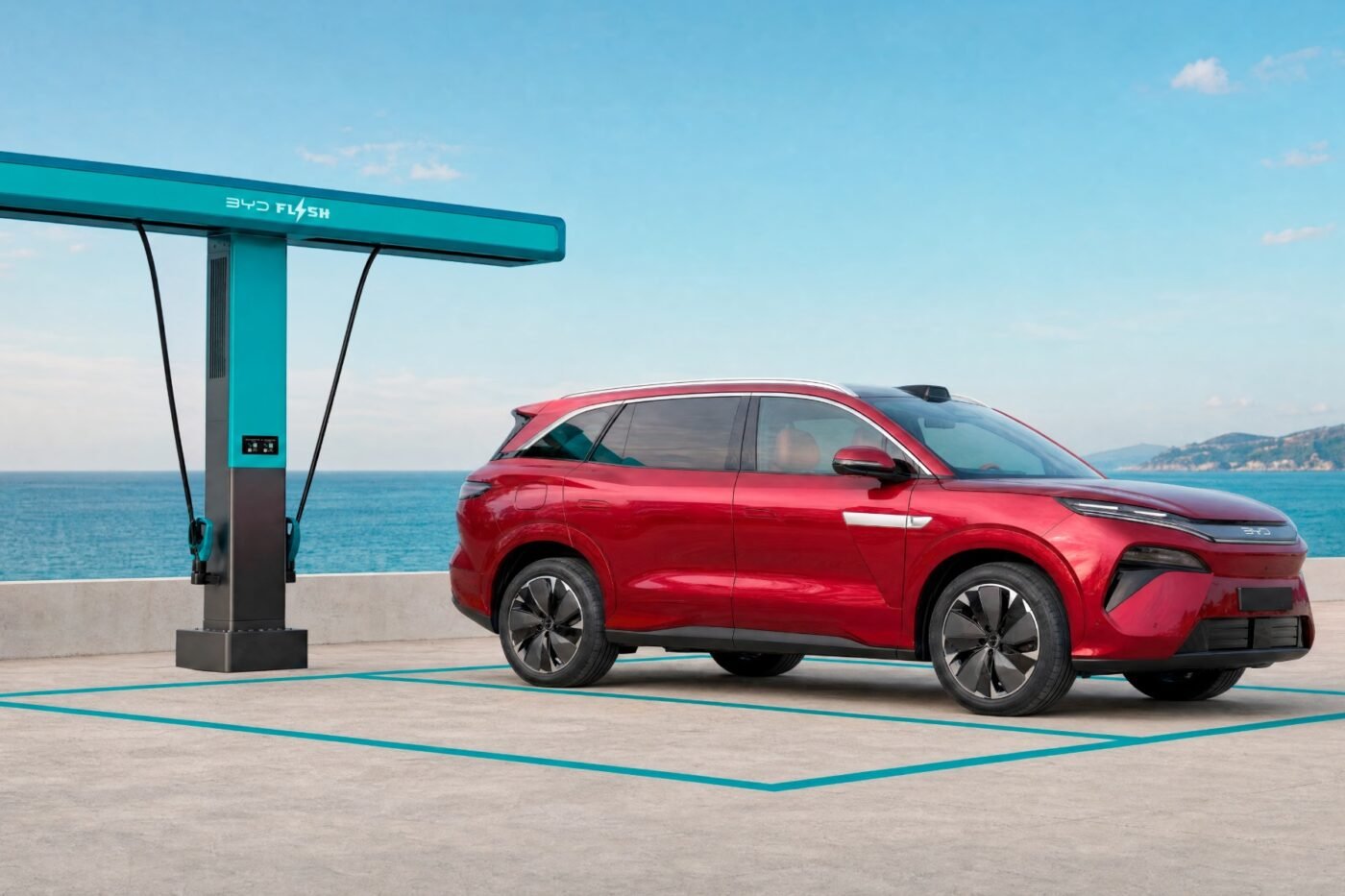 BYD Atto 8 rossa parcheggiata accanto a una colonnina BYD Flash Charging, con il mare sullo sfondo